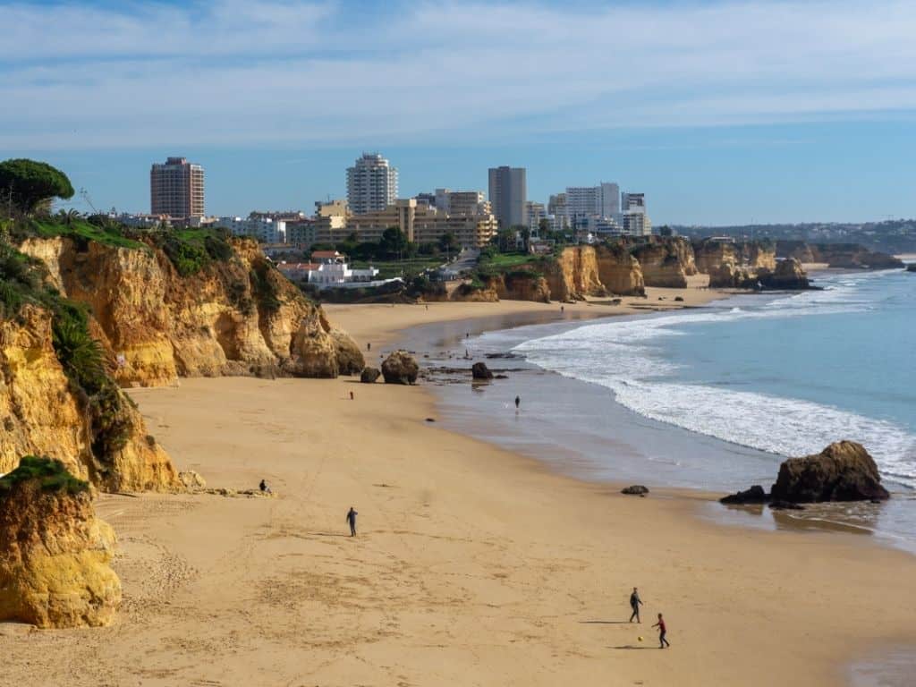 A beach with cliffs in the foreground and a city skyline in the background