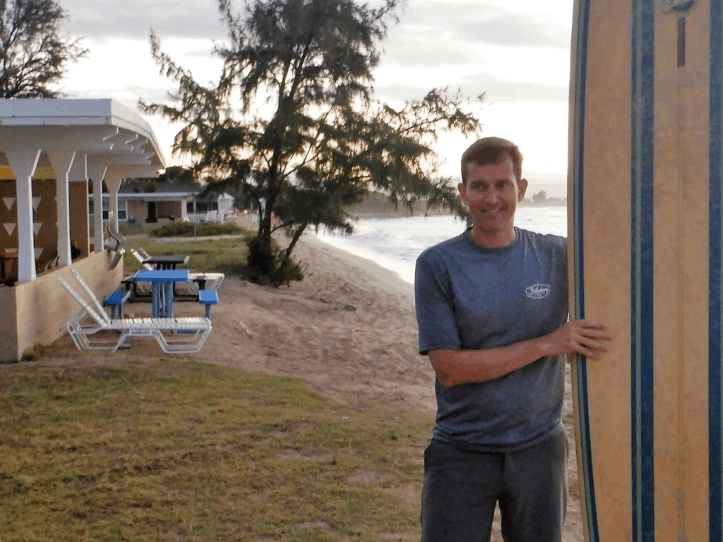 A man standing next to a surf board with the beach in the background
