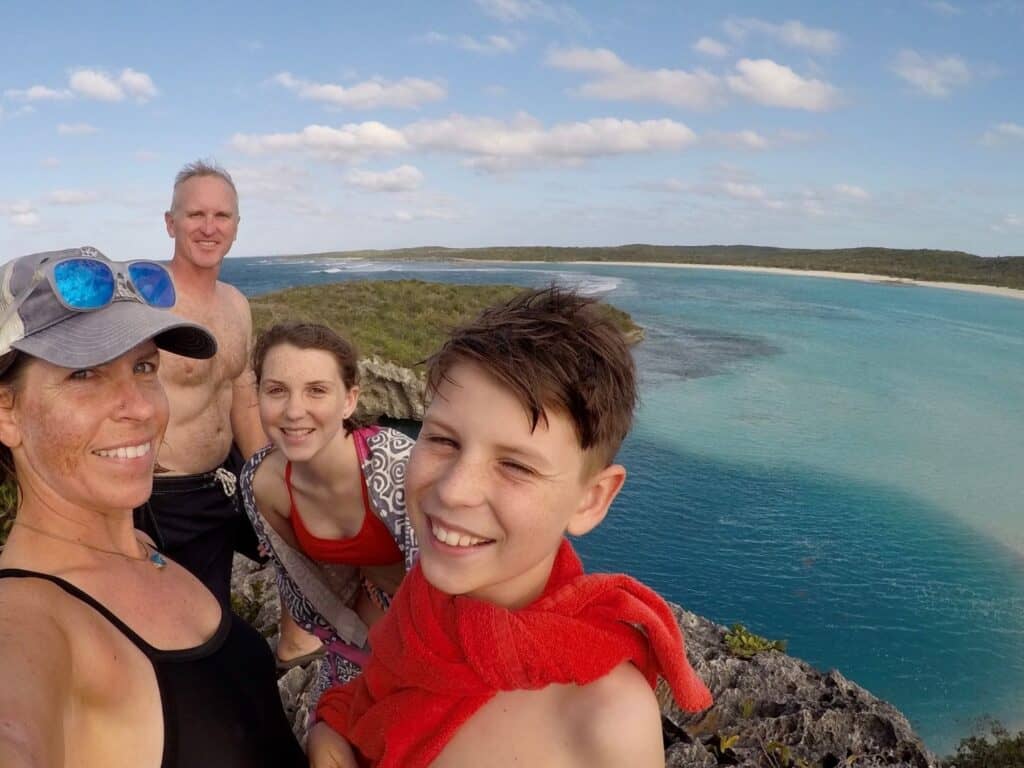 A family taking a selfie on a cliff overlooking bright blue water
