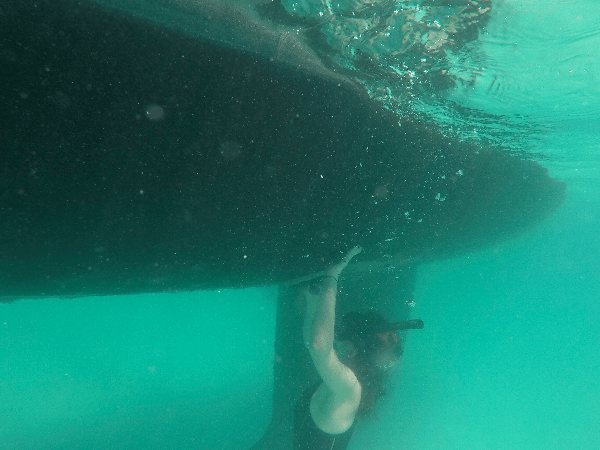 Underwater view of a girl cleaning the bottom of a boat