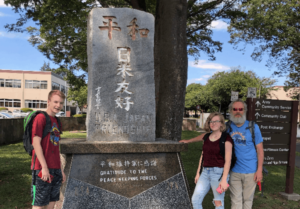Diana's husband and kids next to a stone memorial with Japanese writing.