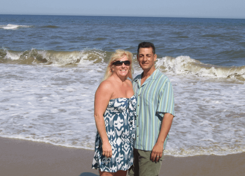 Colleen and Ron standing on the beach with the ocean behind them