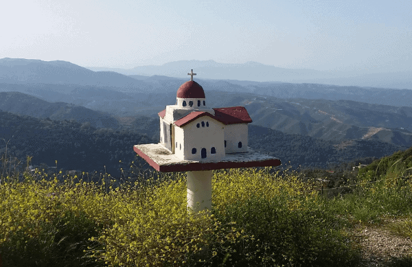 A miniature replica of a Catholic church on a small pedestal with mountains in the background