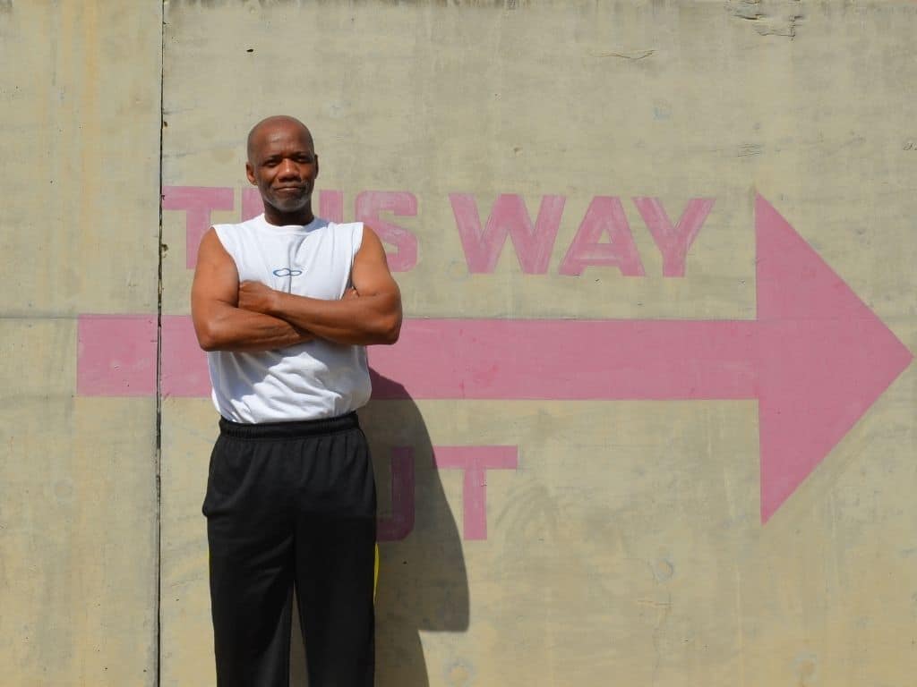 Picture of the interviewee standing in front of a wall with arms crossed.