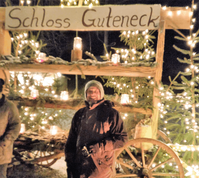 Picture of the interviewee at a Christmas market surrounded by lights and a sign that says Schloss Guteneck