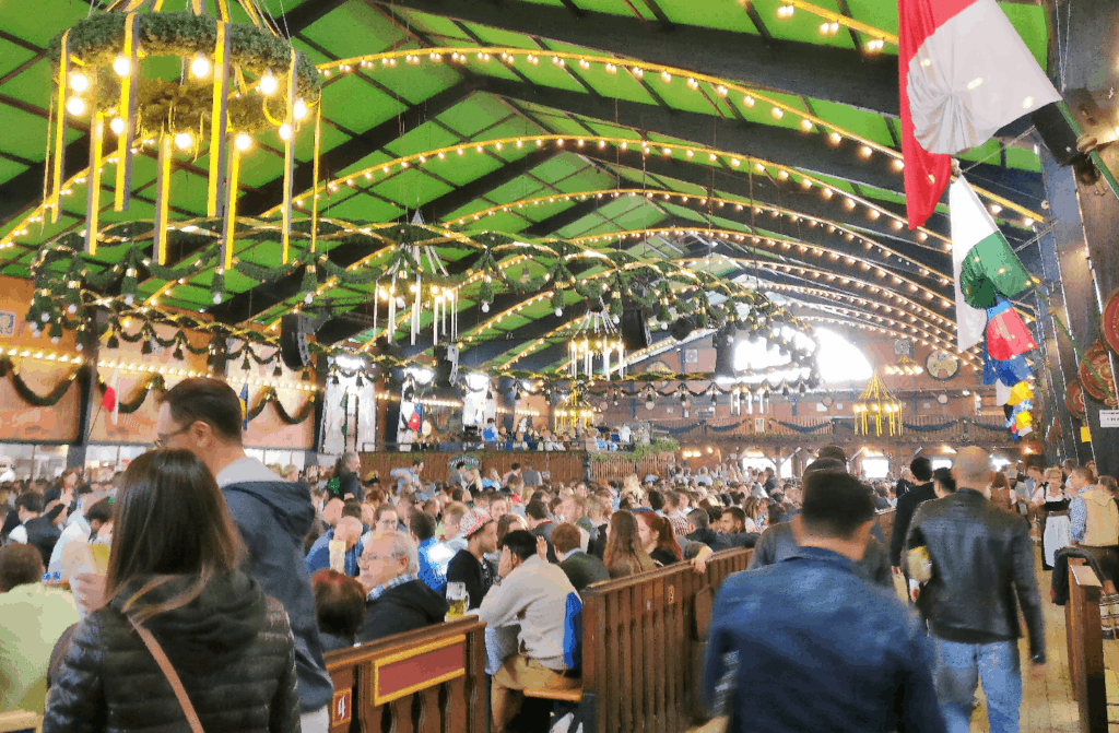 A large, brightly-lit hall with a green ceiling and crowds of people drinking beer.