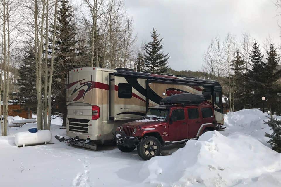 A large motorhome next to a red Jeep at a snowy campground