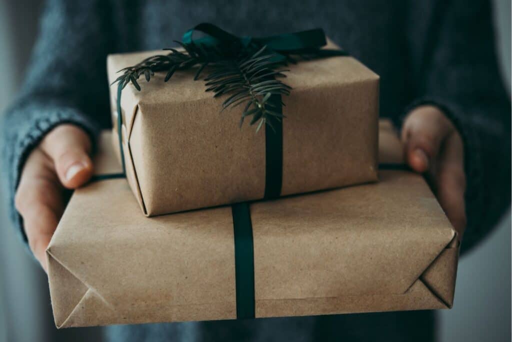 A person's hand holding gifts wrapped in brown paper