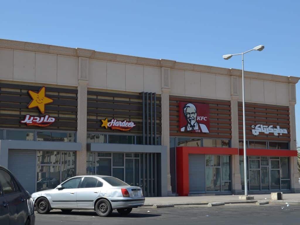 Storefronts of KFC, Hardee's with a car parked in front.