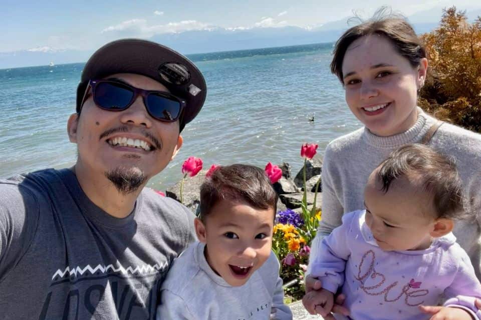 A couple with two young children taking a selfie in front of a lake