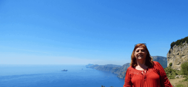 Lisa in a red shirt with a long stretch of the Amalfi Coast behind her