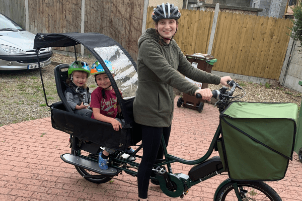 Sara holding the handlebars of a bicycle with two kids in the back.