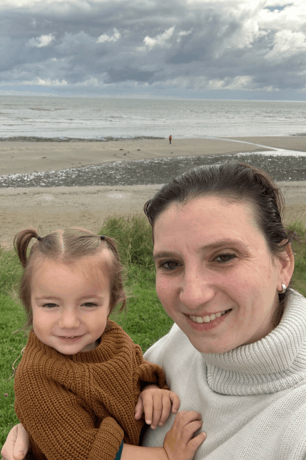 Sara holding her daughter with the beach in the background