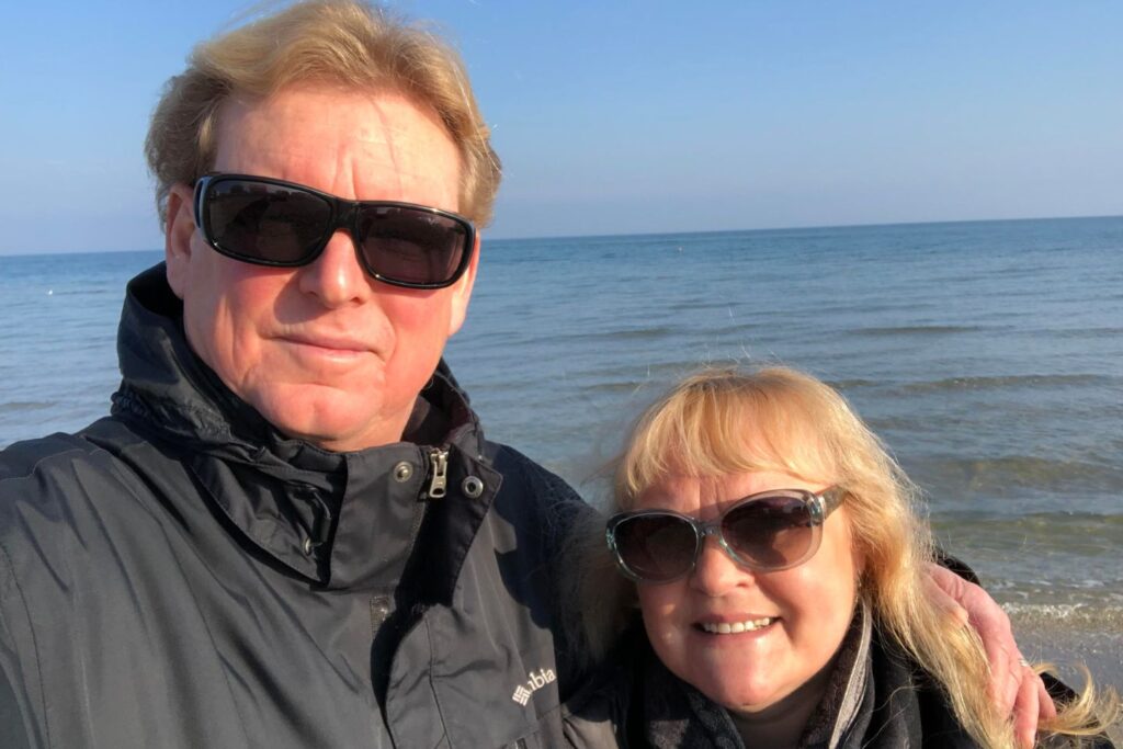 A blonde couple taking a selfie in front of the sea