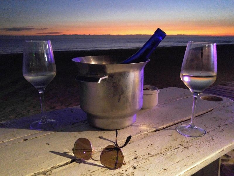 Two wine glass, a chilled bottle of wine, and sunglasses on a table.