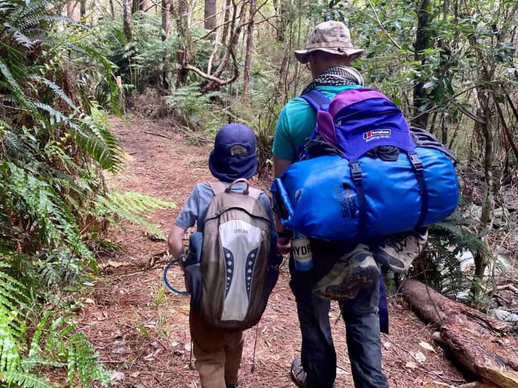A man and his son wearing backpacks and hiking through the woods