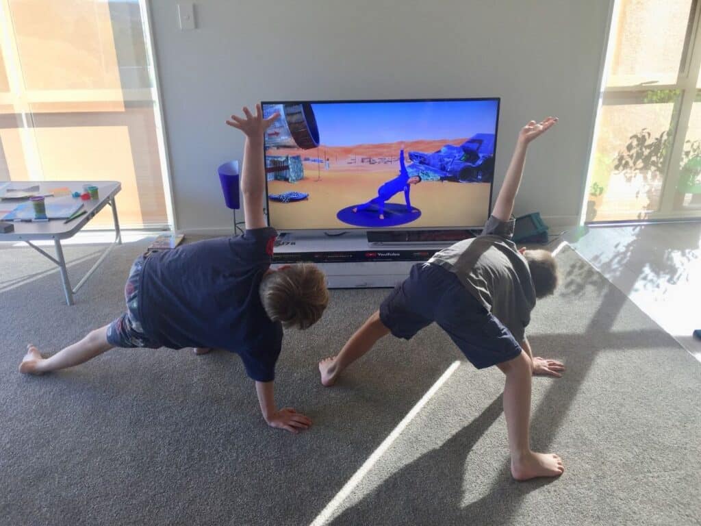 Two young boys following a yoga video on TV