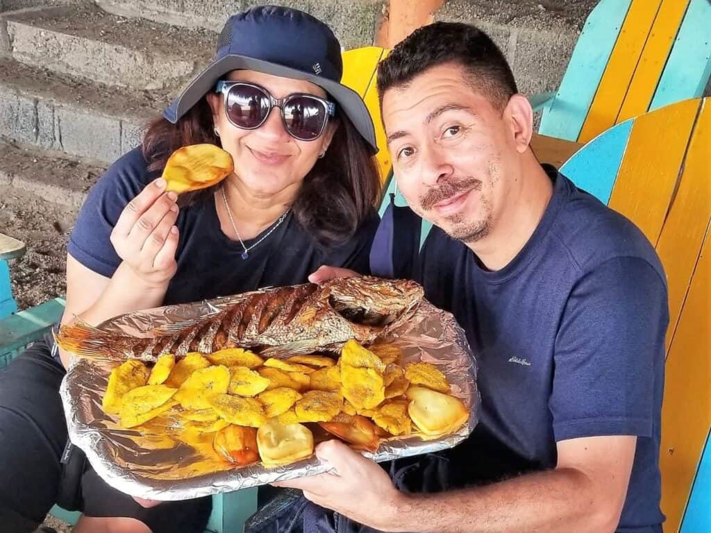 A couple at the beach with a platter of fish and plantains