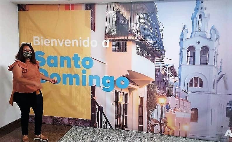 A woman standing in front of a large sign that says Bienvenido a Santo Domingo