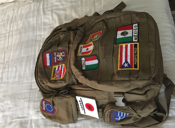 A khaki-colored canvas backpack with patches from various countries