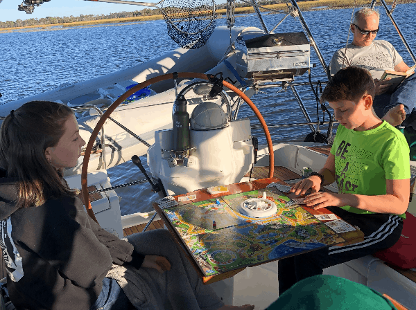 The kids playing a board game on the boat while dad reads in the background