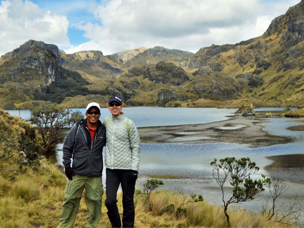 A couple dressed in hiking clothes with water and mountains in the background