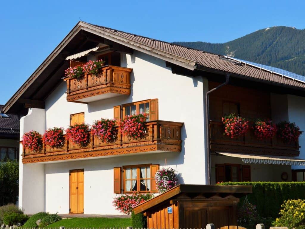 The outside of a white German-style home with balconies lined in flower pots