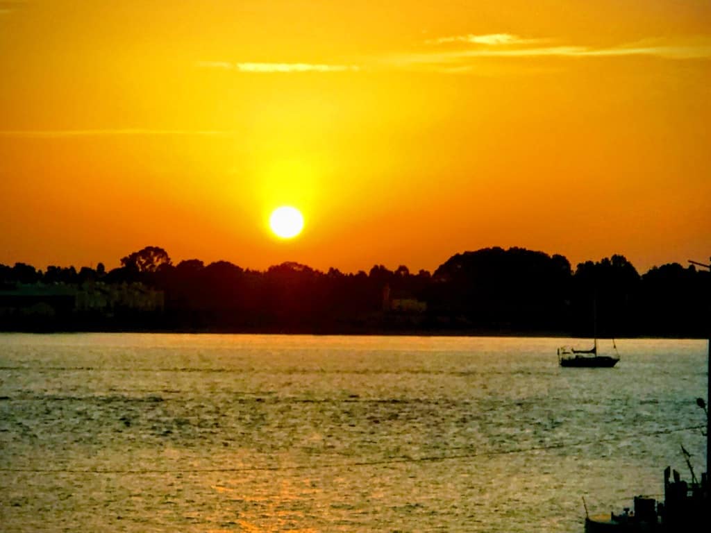 Sunset over a river with a boat and trees in the background