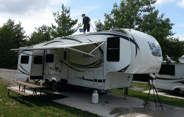 Lisa standing on top of her RV trailer with a bucket and hose in her hands