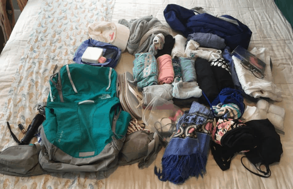 A green backpack with rolled clothes on the bed