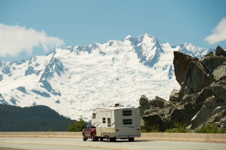 A truck towing a fifth wheel past a snow-covered mountain
