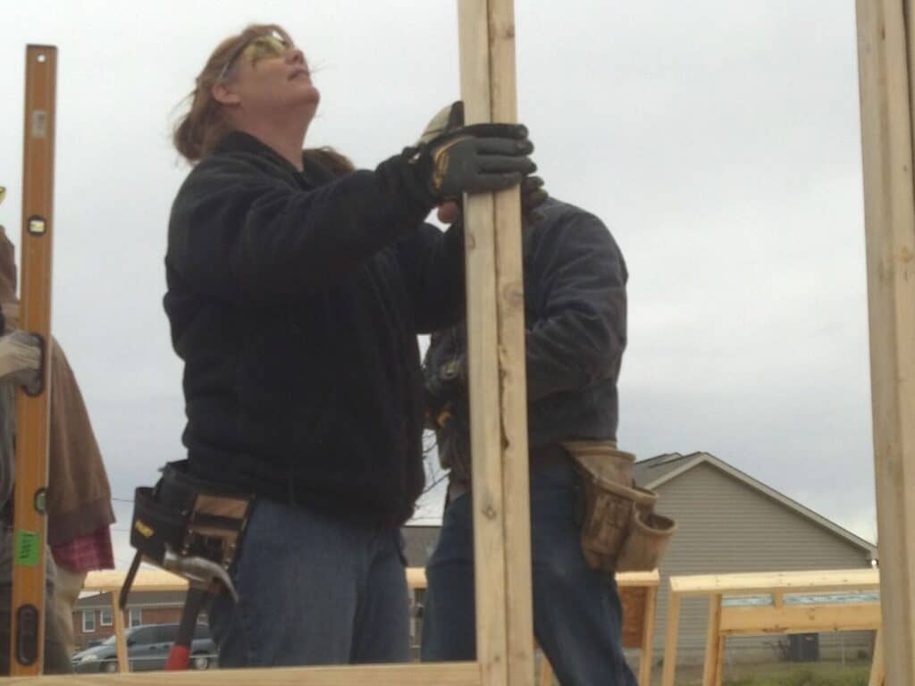 A woman holding a wooden beam while constructing a house