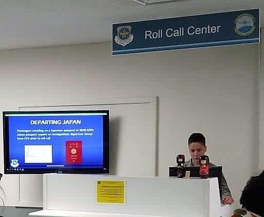 A staff member at the Yokota passenger terminal stands under the Roll Call Center sign to announce the names of Space-A passengers selected for a flight.