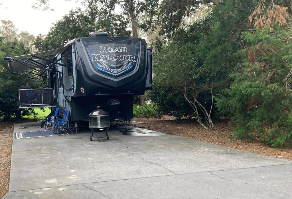 An RV trailer parked on a concrete slab surrounded by trees
