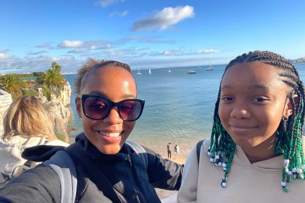 A woman and her teen daughter taking a selfie with the beach in the background