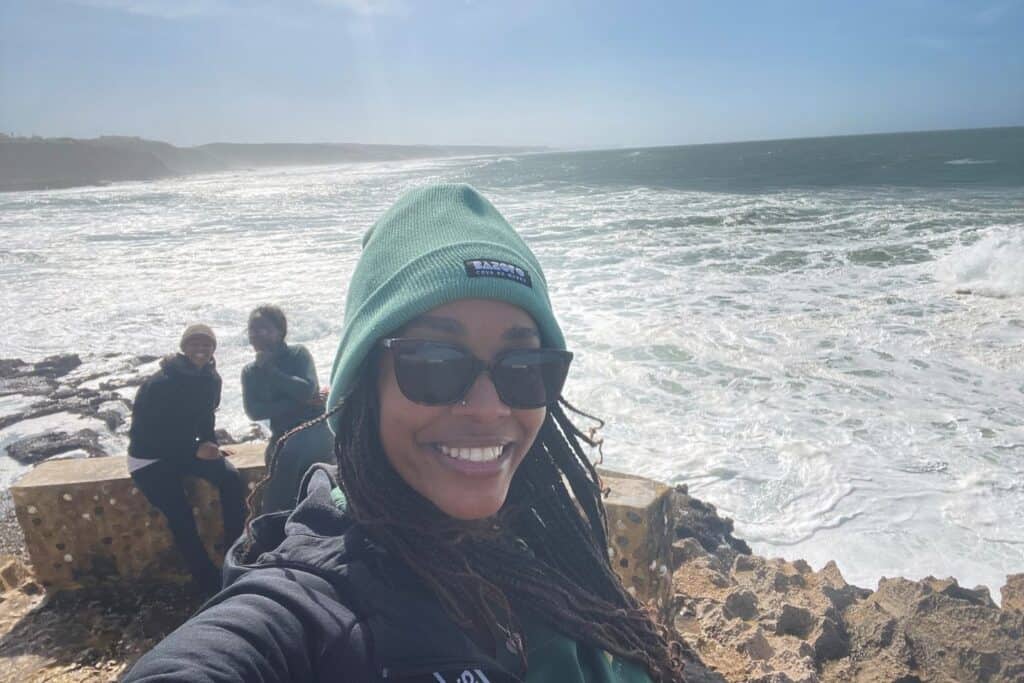 A woman in sunglasses taking a selfie in front of the ocean