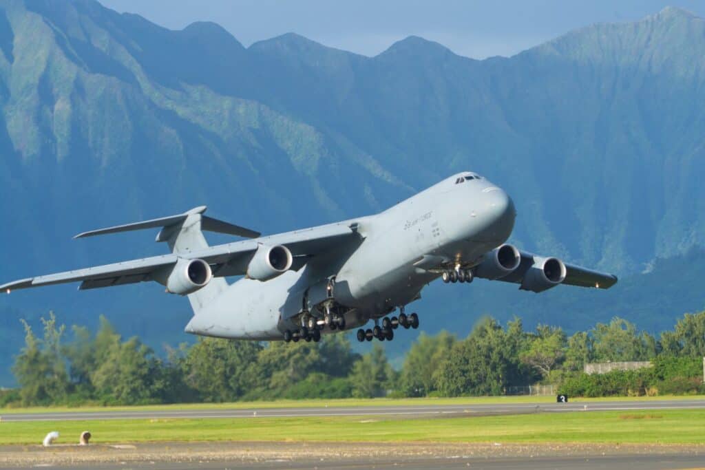 A military cargo plane taking off with mountains in the background